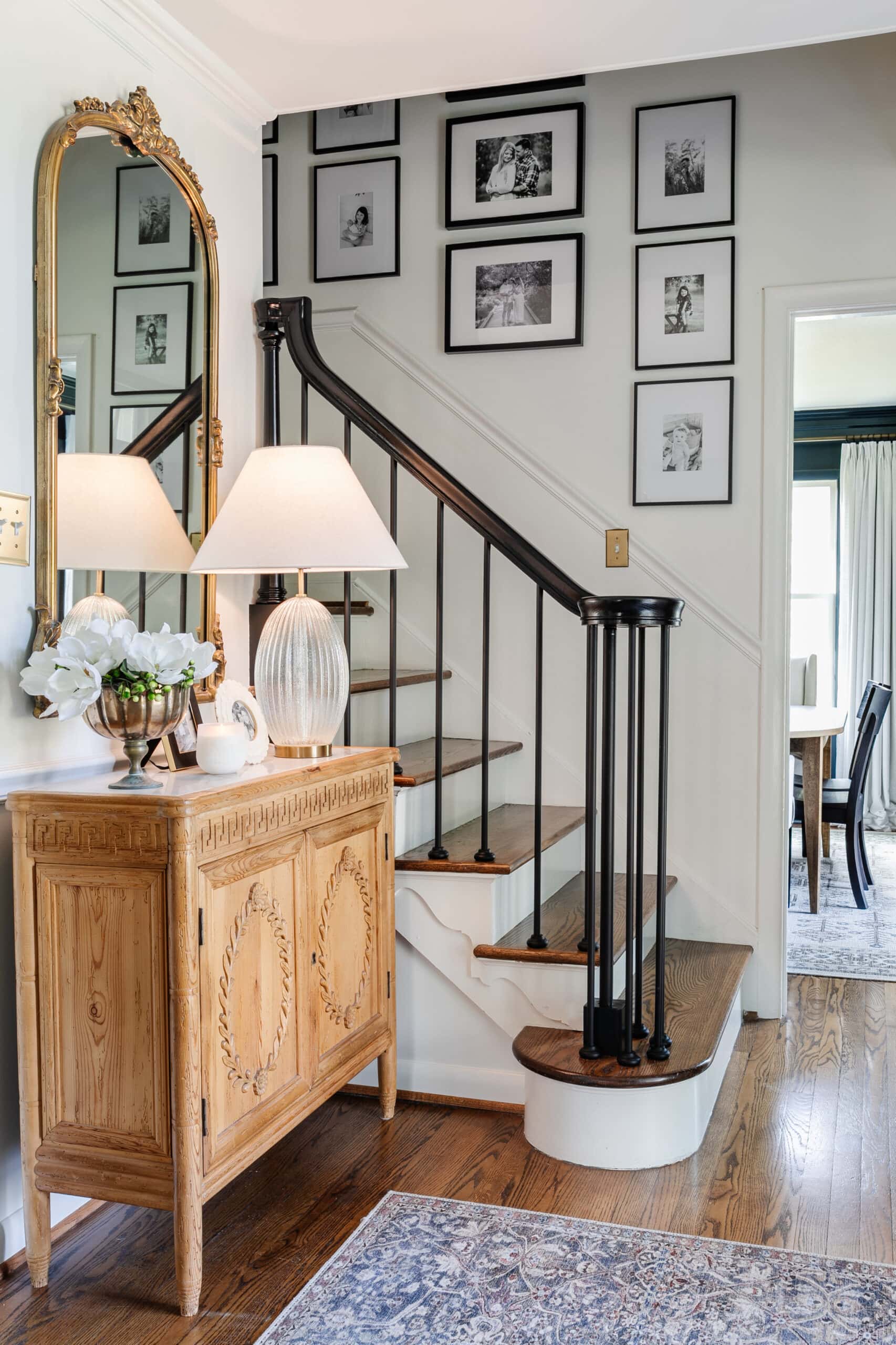 classic foyer with carved wood credenza, black stair railing, and family gallery wall on stairs 