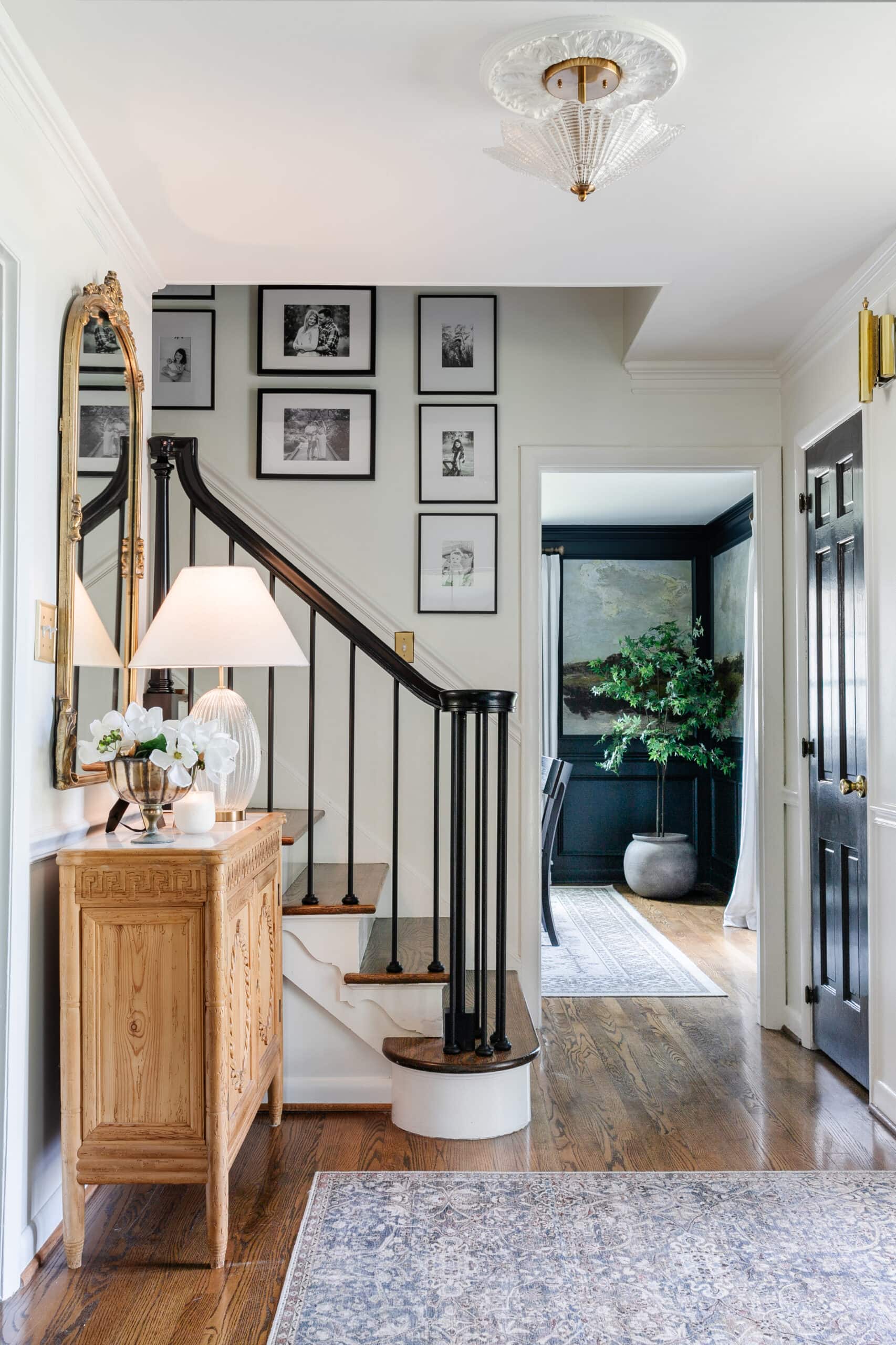 classic foyer with carved wood credenza, black stair railing, and family gallery wall on stairs 