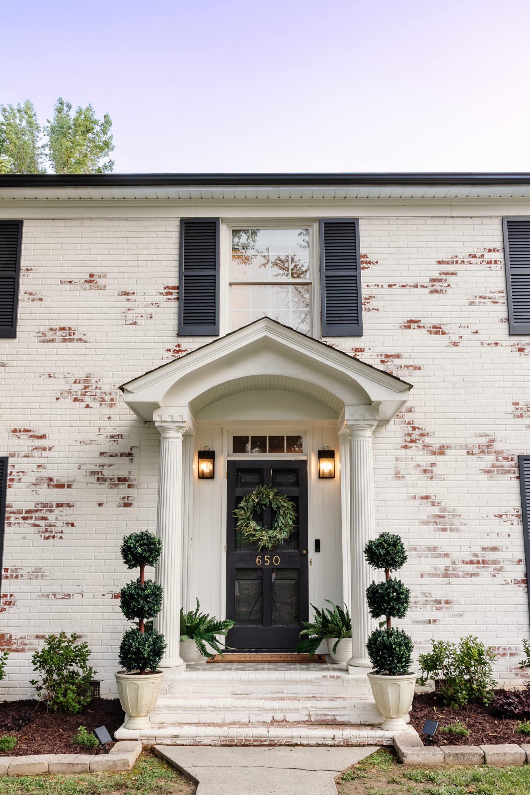 front porch stoop on a colonial house with topiaries, ferns, and wreath