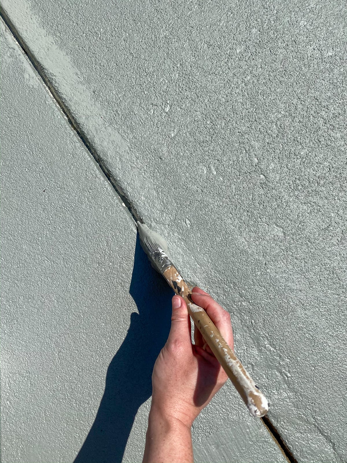 applying concrete paint in cracks and edges to finish a patio